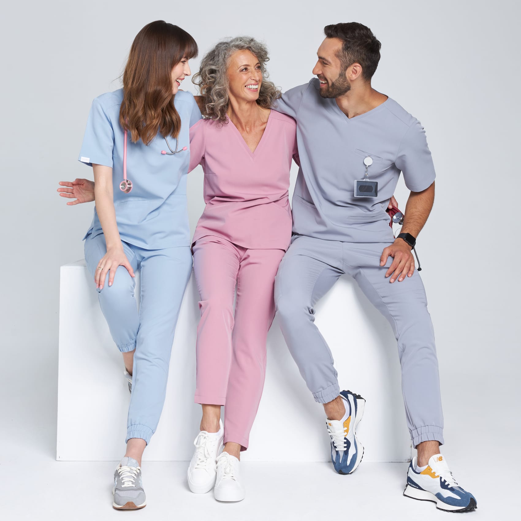 Trójka uśmiechniętych osób w kolorowych uniformach medycznych siedzi razem i rozmawia.