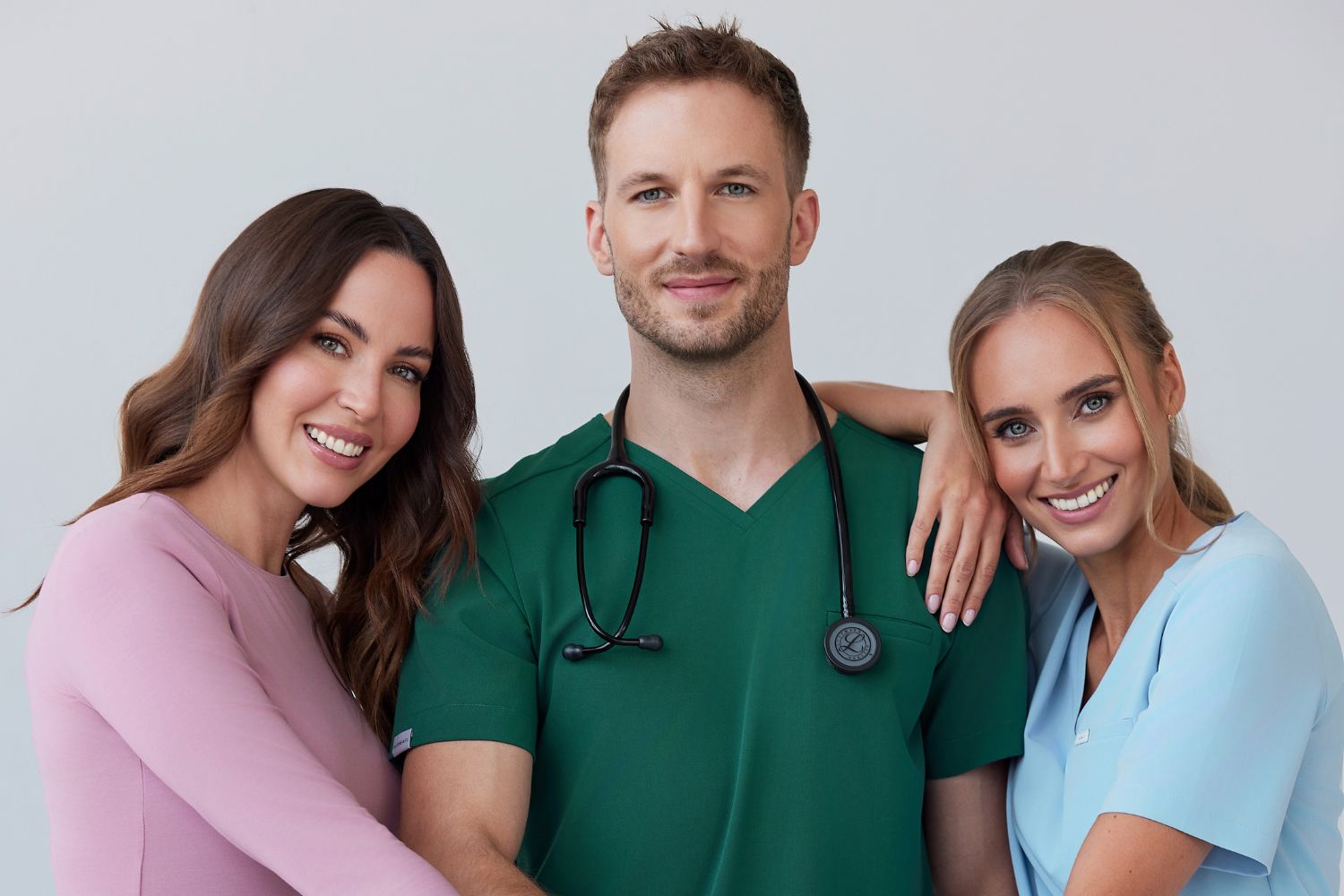 Trzy uśmiechnięte osoby w kolorowej odzieży medycznej.