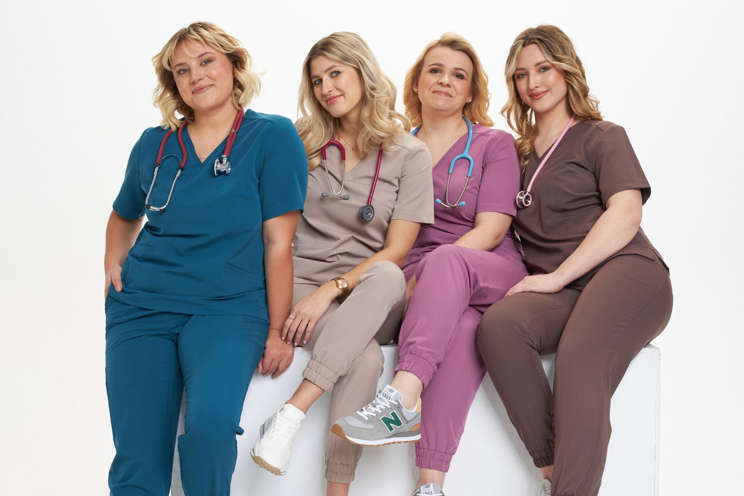 Cztery kobiety w kolorowej odzieży medycznej z stetoskopami pozują uśmiechnięte.